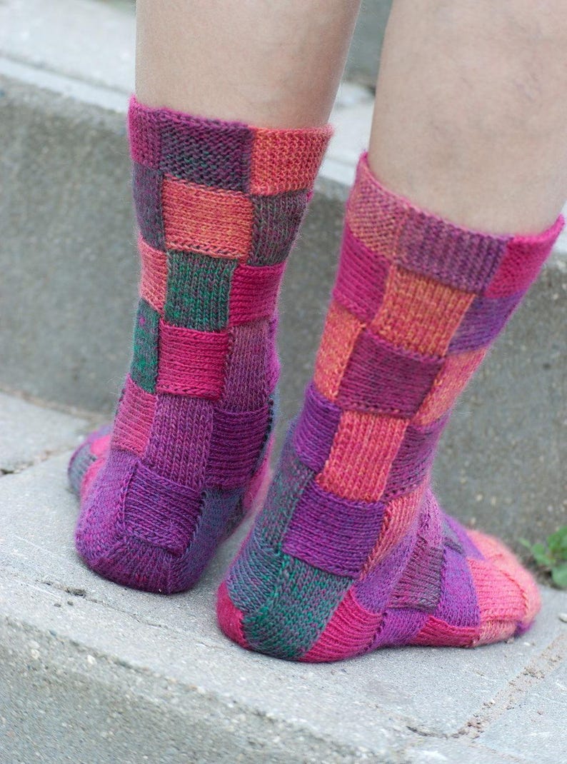 May include: A pair of colorful knitted socks with a patchwork design in shades of pink, purple, green, and orange.