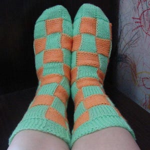 May include: A pair of green and orange checkered socks. The socks are knitted with a checkerboard pattern.