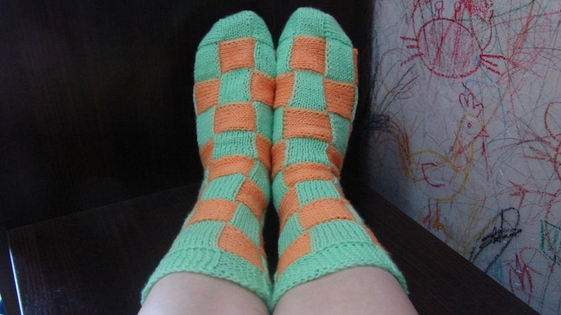 May include: A pair of green and orange checkered socks. The socks are knitted with a checkerboard pattern.