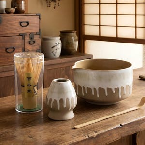May include: A collection of Japanese tea ceremony tools, including a bamboo whisk in a clear container, a ceramic bowl with a dripped glaze, a small ceramic vase, and a bamboo scoop. The items are arranged on a wooden surface.