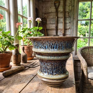 May include: A ceramic planter featuring a wide, flared rim and a tapered body with a glossy glaze in shades of brown, tan, and blue. The surface displays a distinctive drip pattern that creates vertical streaks of colour across the exterior.