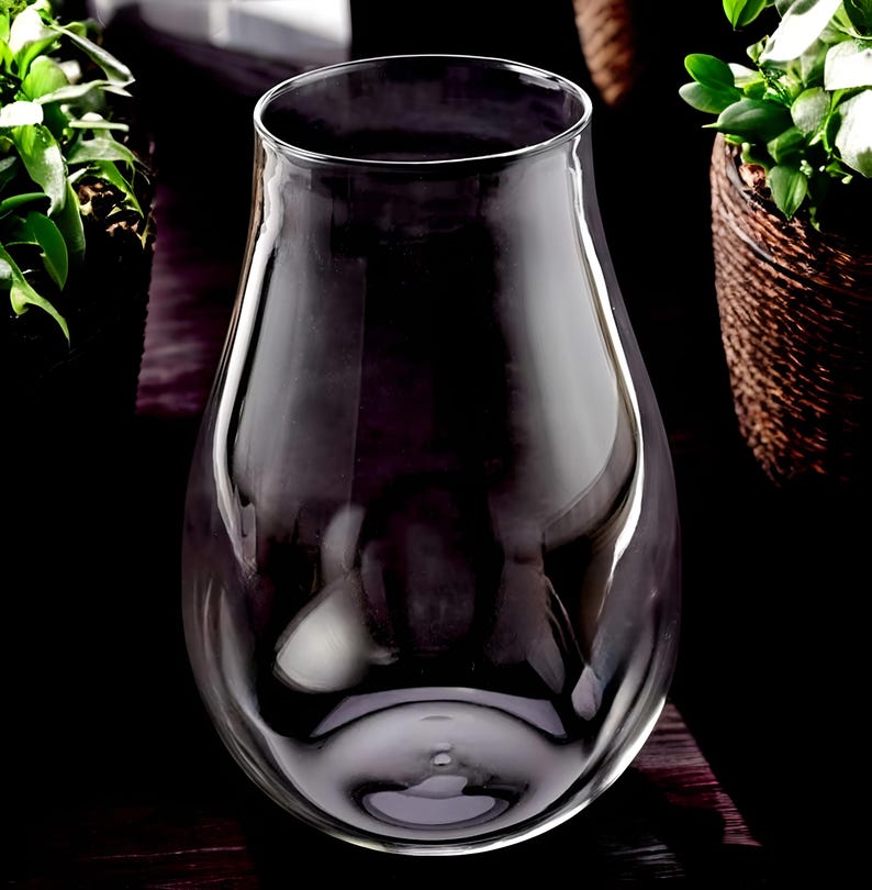 May include: A clear glass vase with a wide, round base and a narrow neck. The vase is empty and has a smooth, polished surface.