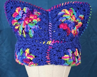 May include: A blue crocheted hat with a colorful butterfly design. The hat is on a white mannequin head.