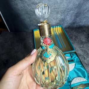 Puede incluir: Un frasco de perfume de vidrio transparente con dise&ntilde;o acanalado, cuello dorado y tap&oacute;n transparente retorcido. El frasco presenta un sello de cera roja y una etiqueta dorada con el texto 4711. Se presenta en una caja turquesa con dos jabones redondos.