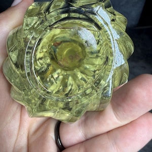 Puede incluir: Un objeto de vidrio transl&uacute;cido de color amarillo p&aacute;lido con una forma geom&eacute;trica facetada en forma de estrella. La base presenta una hendidura circular con el n&uacute;mero 0196 grabado en el centro. El vidrio tiene una superficie lisa y brillante.