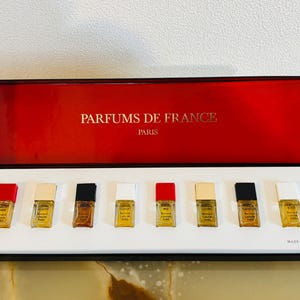 May include: A set of miniature perfumes in a black and red box. The box is labeled "PARFUMS DE FRANCE PARIS" in gold lettering. The set includes seven small perfume bottles with different colored caps.