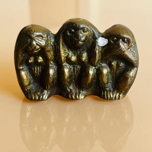 May include: Three small, gold-colored monkeys, each with a different gesture: one covering its eyes, one covering its ears, and one covering its mouth. The monkeys are sitting side-by-side.