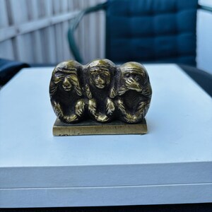 May include: Three brass monkeys, each covering a different sense: see no evil, hear no evil, speak no evil. The monkeys are sitting on a small, rectangular base.