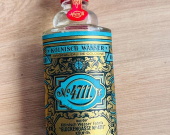 Puede incluir: Una botella de vidrio transparente de 4711 Original Eau de Cologne. La botella tiene una tapa dorada y una etiqueta con detalles en azul y dorado. La etiqueta dice "KÖLNISCH WASSER" y "No. 4711".