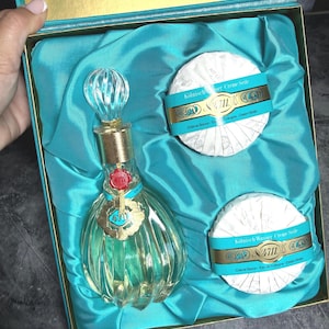 Puede incluir: Un set de regalo 4711 Echt Kolnisch Wasser en una caja color verde azulado que contiene una botella de vidrio de colonia con dise&ntilde;o acanalado, tapa dorada y sello de cera roja, junto a dos pastillas de jab&oacute;n crema redondas envueltas en papel blanco.