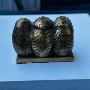 May include: A bronze sculpture of three abstract figures, each with a textured surface, sitting on a rectangular base.