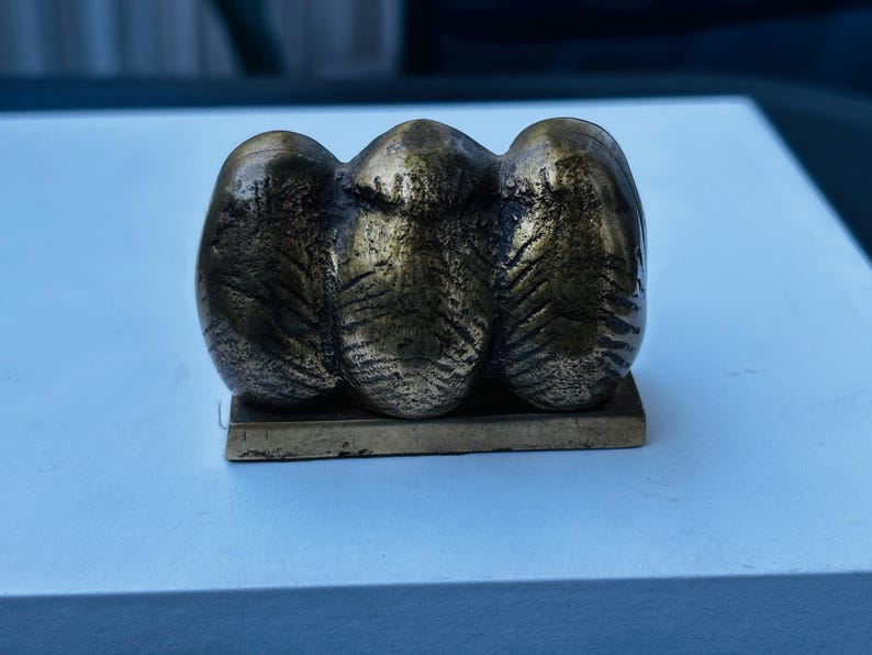 May include: A bronze sculpture of three abstract figures, each with a textured surface, sitting on a rectangular base.