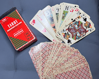 Puede incluir: Una baraja de 78 cartas de tarot con una caja roja y verde. Las cartas están abanicadas, mostrando varios palos e ilustraciones. Los dorsos de las cartas tienen un patrón de cuadros rojos y marrones. La caja dice "TAROT" y "78 cartes plastifiées lavables".