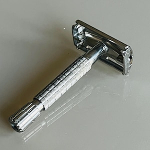 Puede incluir: Una maquinilla de afeitar de seguridad plateada con un mango texturizado y una cabeza cromada.