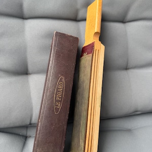 Puede incluir: Un afilador de navajas antiguo de madera con una funda de cuero marrón. El afilador es de madera y cuero, con un mango. La funda es rectangular y tiene la inscripción "LE FIGARO".