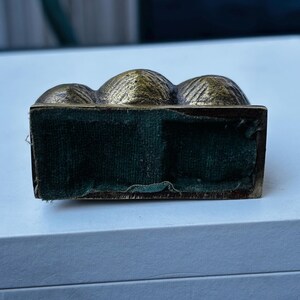 May include: A small, gold-colored metal box with a velvet lining. The box is shaped like three rounded mounds.