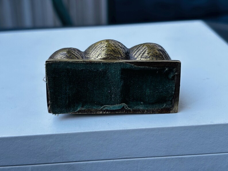 May include: A small, gold-colored metal box with a velvet lining. The box is shaped like three rounded mounds.