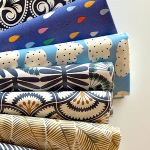 May include: A stack of eight fabric squares with different patterns. The patterns include floral, geometric, and abstract designs. The fabrics are in shades of blue, black, white, and gold.