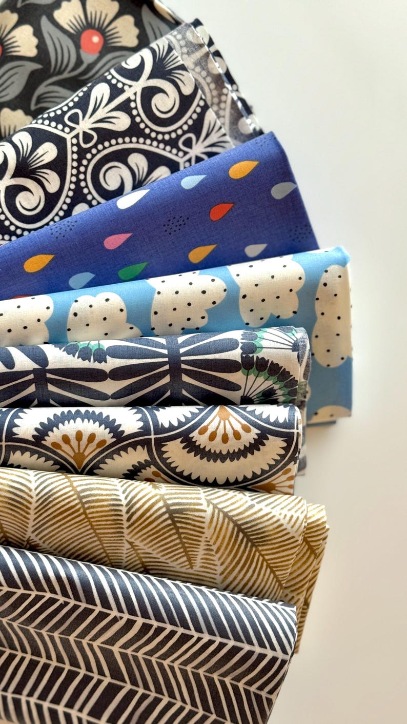 May include: A stack of eight fabric squares with different patterns. The patterns include floral, geometric, and abstract designs. The fabrics are in shades of blue, black, white, and gold.