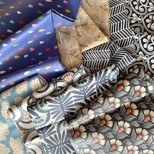 May include: A collection of fabric swatches in various patterns and colors, including blue, black, white, and gold. The fabrics feature geometric, floral, and abstract designs.