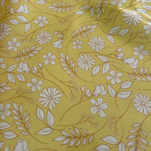 May include: A yellow fabric featuring a repeating pattern of white line-drawn flowers, leaves, and small berries. The design consists of various floral stems and foliage arranged across the surface, creating a continuous botanical print.