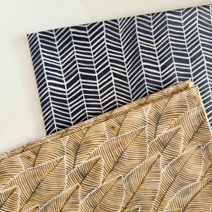 May include: Two fabric swatches with different patterns. One swatch is a dark blue fabric with a white chevron pattern. The other swatch is a light beige fabric with a brown leaf pattern.