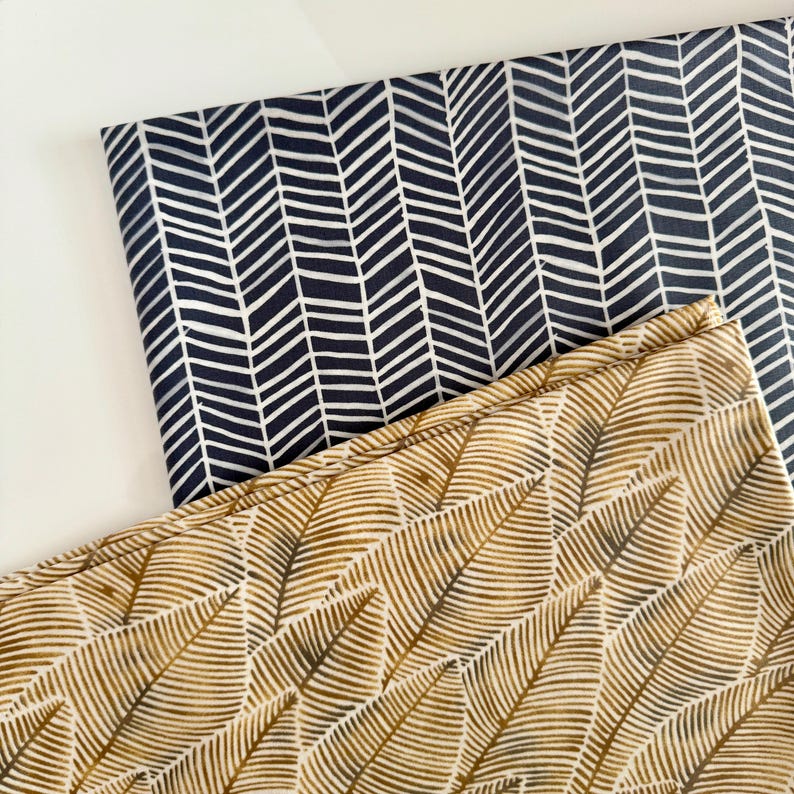 May include: Two fabric swatches with different patterns. One swatch is a dark blue fabric with a white chevron pattern. The other swatch is a light beige fabric with a brown leaf pattern.
