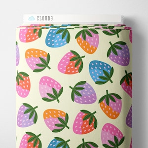 May include: A bolt of fabric featuring a repeating pattern of stylized strawberries in shades of pink, orange, blue, and purple on a cream background. Each strawberry has green leaves and white seeds. The top edge displays the text CLOUD9.