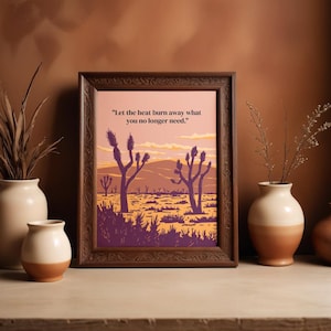May include: A framed art print featuring a desert landscape with Joshua trees in shades of purple, orange, and yellow. The print includes the quote, "Let the heat burn away what you no longer need." The frame is a dark brown color.