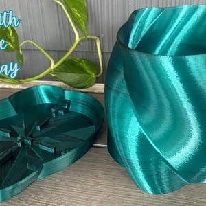 May include: A teal-colored planter with a matching drip tray. The planter has a unique, swirling design. The drip tray is oval-shaped with a starburst pattern. Text on the image reads "Planter with Drainage & Drip Tray."