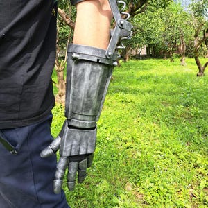 May include: A metallic gray prosthetic arm, featuring a gauntlet and forearm design. The arm is articulated with hinges and straps for attachment. The overall aesthetic suggests a steampunk or fantasy theme.