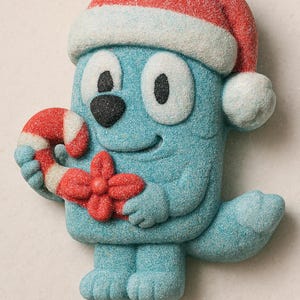 Può includere: Un personaggio azzurro, ricoperto di zucchero, con un cappello da Babbo Natale rosso e bianco, che tiene in mano un bastoncino di zucchero rosso e bianco e un fiocco rosso. Il personaggio ha grandi occhi neri e un naso nero, con un'espressione sorridente. Decorazione natalizia.