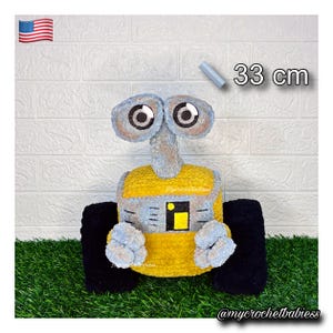May include: A plush toy robot featuring a yellow and grey body, two large circular eyes, and black treads. The robot has a textured surface and measures 33 cm in height. The design includes a small yellow and black square detail on the front.