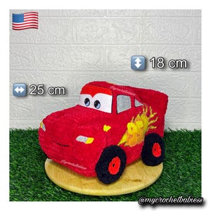 Può includere: Un'auto di peluche rossa con occhi bianchi, fari gialli e una grafica a fiamma gialla con il numero 95 sul lato. Il giocattolo misura 25 cm di lunghezza e 18 cm di altezza. Presenta ruote nere con centri rossi e finestrini grigi.