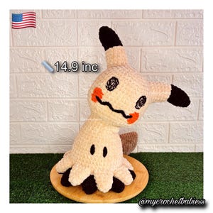May include: A beige crochet plush toy, approximately 14.9 inches tall, with black ears, eyes, and feet. The toy has an orange mouth and cheeks. It is sitting on a wooden round base.