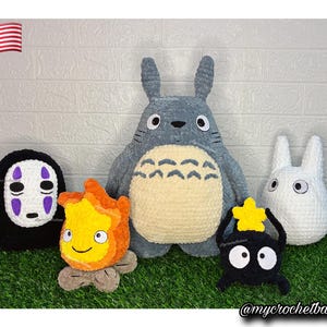 Op de afbeelding: Een verzameling van vijf handgemaakte gehaakte knuffels, waaronder een grote grijze Totoro, een kleine witte Totoro, een zwart Gezichtloos personage, een oranje en gele vlamfiguur en een zwart roetwezentje met een gele ster op zijn hoofd.