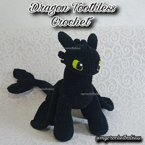 May include: A black crochet dragon toy with yellow eyes and a long tail. The text "Dragon Toothless Crochet" is above the dragon. The dragon is made of soft yarn and has a friendly appearance. The dragon is a handmade item.