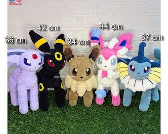 May include: Five plush crochet creatures standing in a row. From left to right: a light purple creature at 36 cm, a black creature with yellow rings at 42 cm, a brown creature at 34 cm, a pink and white creature at 44 cm, and a blue creature at 37 cm.