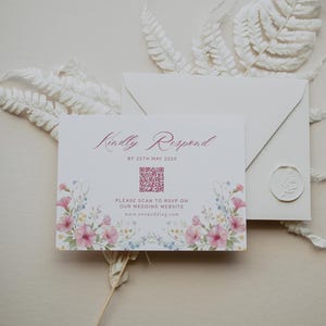 May include: A wedding invitation suite featuring a card with floral accents and the text "Kindly Respond." The card includes a QR code and website address. An envelope and decorative fern complete the arrangement.