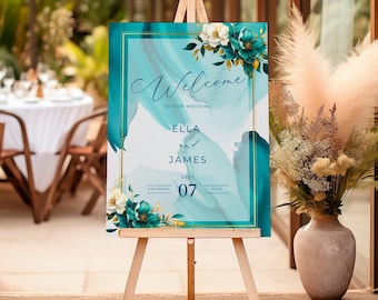 以下が含まれることがあります： 白い花と「Welcome to our wedding Ella and James Saturday Sept 07 20XX」の文字が書かれた、ターコイズブルーとゴールドの結婚式のウェルカムサインです。
