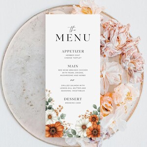 Könnte beinhalten: Eine rechteckige Menükarte mit dem Text "the MENU" oben. Das Menü listet eine Vorspeise, einen Hauptgang und ein Dessert auf. Die Karte ist mit orangefarbenen und weißen Blumen und Grün dekoriert. Die Karte liegt auf einem silbernen Teller mit floralen Akzenten.