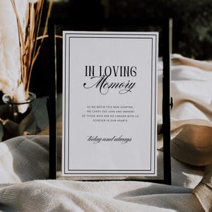 Könnte beinhalten: Ein schwarz gerahmtes Schild mit den Worten "IN LOVING Memory" in eleganter Schrift. Das Schild enthält den Text "AS WE BEGIN THIS NEW CHAPTER...FOREVER IN OUR HEARTS. today and always" auf weißem Hintergrund.