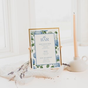 Elegant blue hydrangea wedding bar menu sign featuring soft blue hydrangea florals and greenery surrounding a classic framed drink menu layout. Floral bar menu sign designed for wedding receptions, garden weddings, and elegant outdoor celebrations. Editable and printable Canva template perfect for hydrangea themed weddings, blue floral wedding decor, signature drink menus, and sophisticated wedding bar signage.