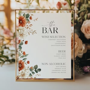 May include: A gold-framed sign with the text "The BAR" and drink selections: wine, beer, and non-alcoholic beverages. The sign is decorated with watercolor floral arrangements in shades of orange, white, and green.