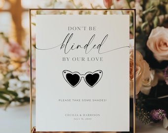 May include: A framed wedding sign with the text "DON'T BE blinded BY OUR LOVE" and "PLEASE TAKE SOME SHADES!". The sign features heart-shaped sunglasses and the names Cecilia & Harrison, with the date July 15, 20XX.