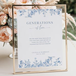 May include: A framed sign with the text "GENERATIONS of love" in navy blue script. The sign has a floral design in blue and white. The text below reads "WE ARE HERE TODAY BECAUSE OF THE LOVE THAT CAME BEFORE US. THANK YOU FOR LAYING THE FOUNDATION FOR OUR FOREVER."