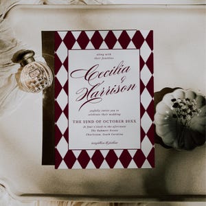 May include: A wedding invitation with a burgundy and white diamond pattern border. The invitation features the names "Cecilia & Harrison" in elegant script, along with event details. A perfume bottle and a decorative dish are also present.