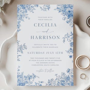 Op de afbeelding: Een blauw-witte huwelijksuitnodiging met bloemmotieven. De uitnodiging vermeldt "Cecilia en Harrison", de datum "Zaterdag 15 juli" en de locatie "The Oakmere Estate, Charleston, South Carolina".