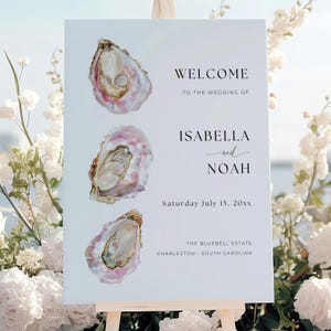 May include: A wedding welcome sign featuring three watercolor oyster illustrations with pink and gold hues. The sign welcomes guests to Isabella and Noah's wedding, with the date and location details.
