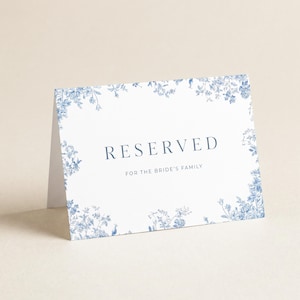 May include: A white card with blue floral border and text that reads "RESERVED FOR THE BRIDE'S FAMILY". The card is folded and stands upright, perfect for wedding or event table settings.